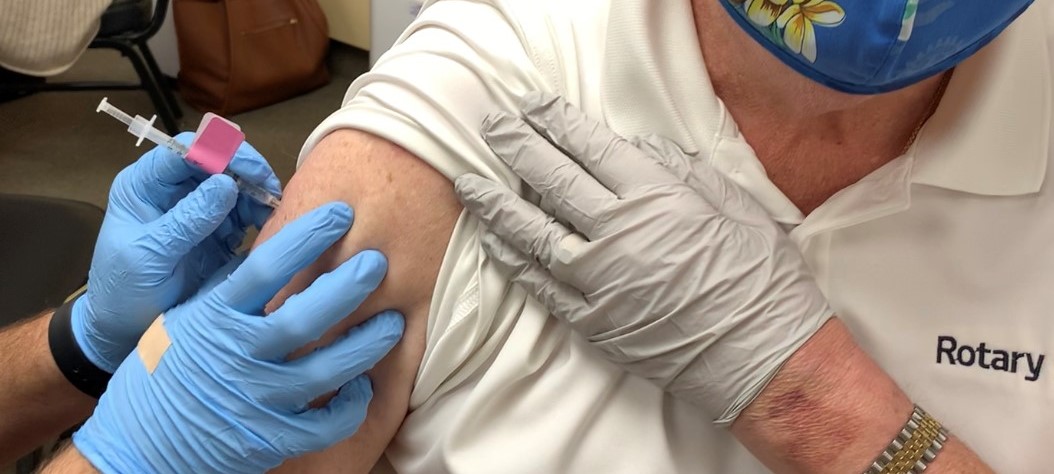 A closeup view of a person's arm accepting a COVID-19 vaccine from a nurse's hands.