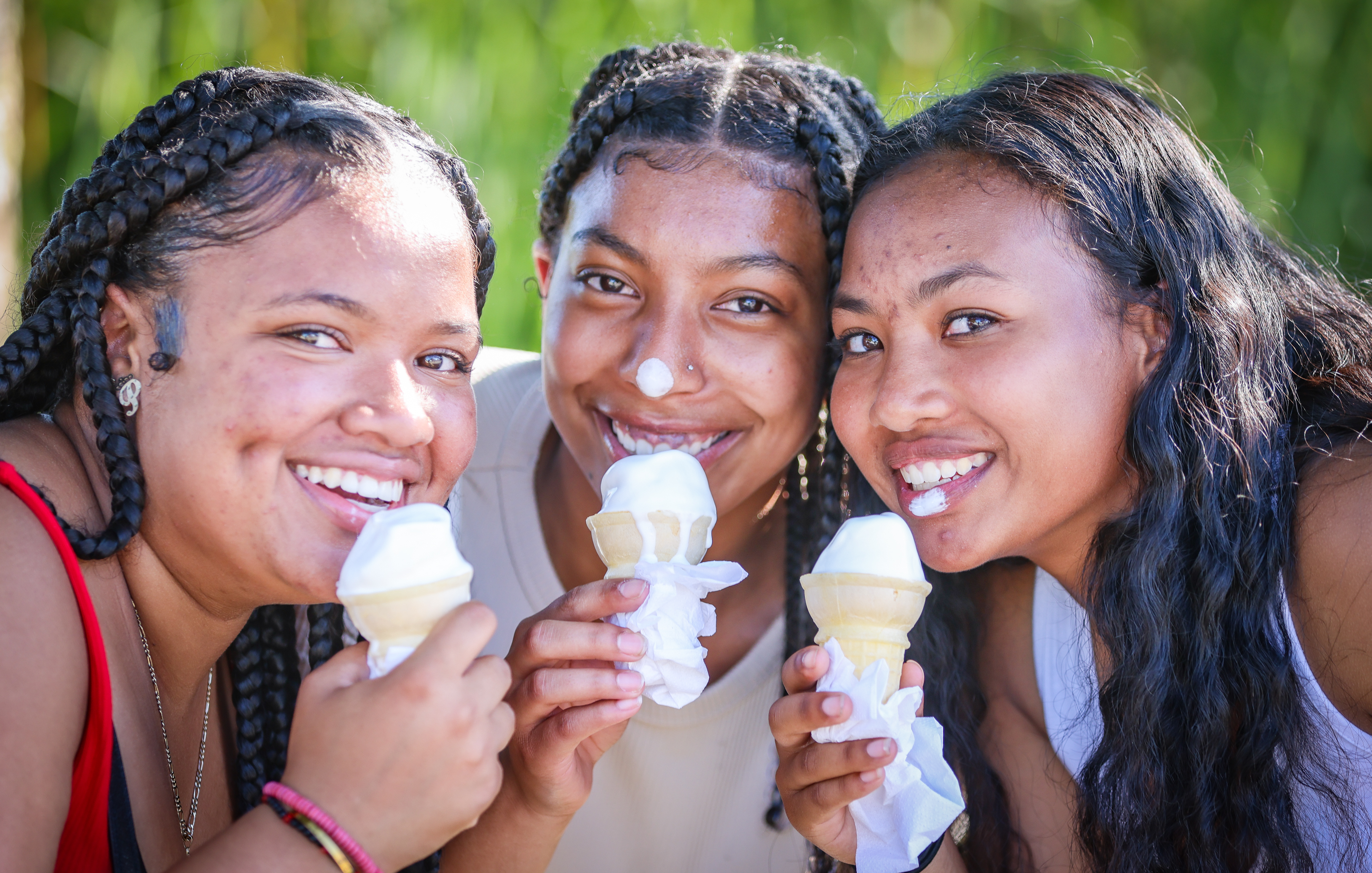 Three teenage girls hold up ice cream cones and smile during the fair.