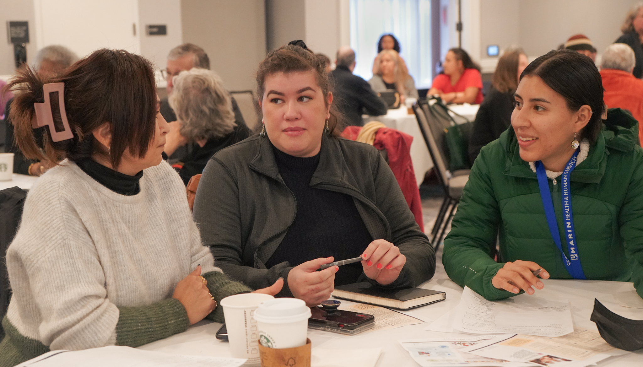Three women sit at a table during an informational session on participatory budgeting.