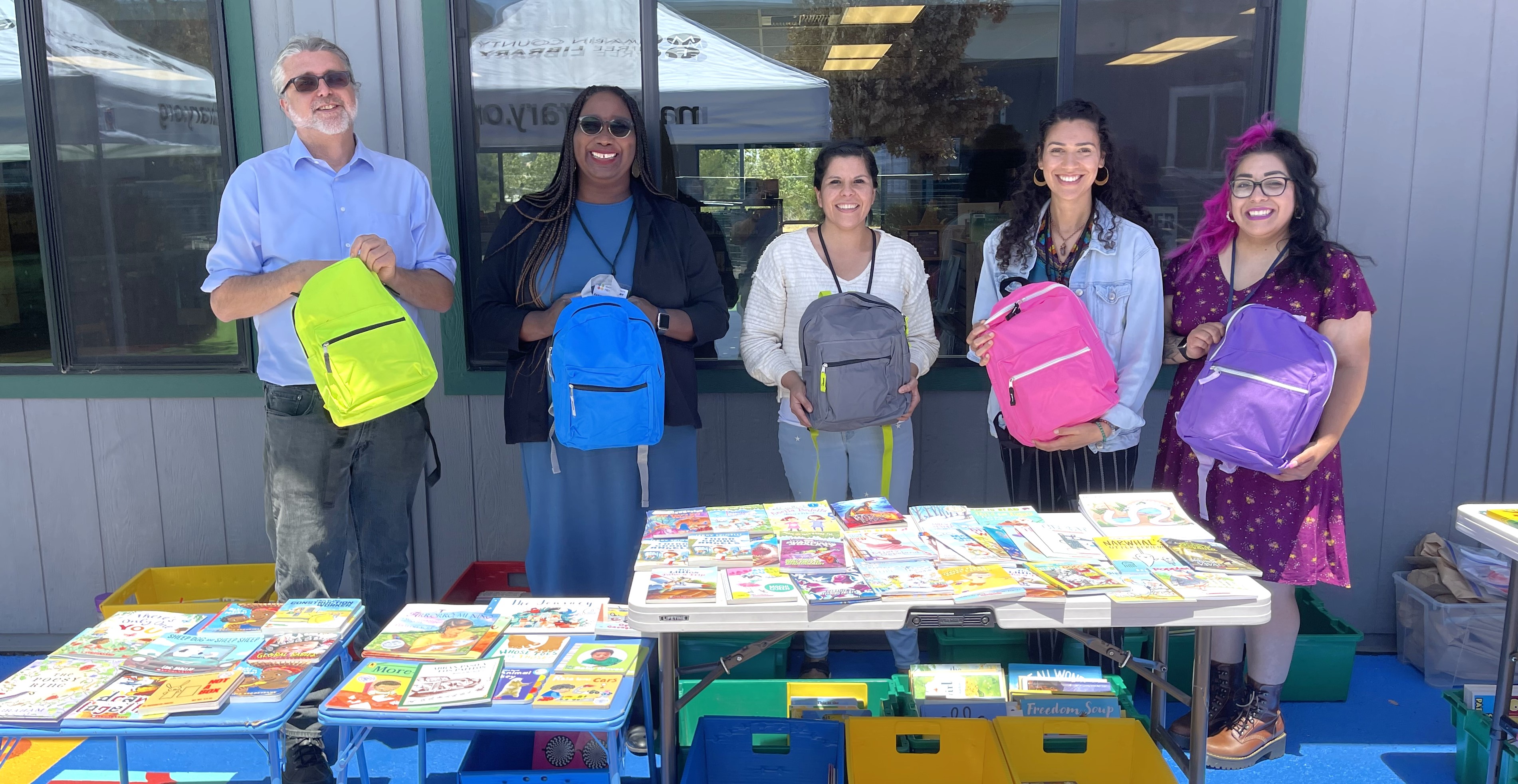 Five library workers smile and pose with children's backpacks to be given away.