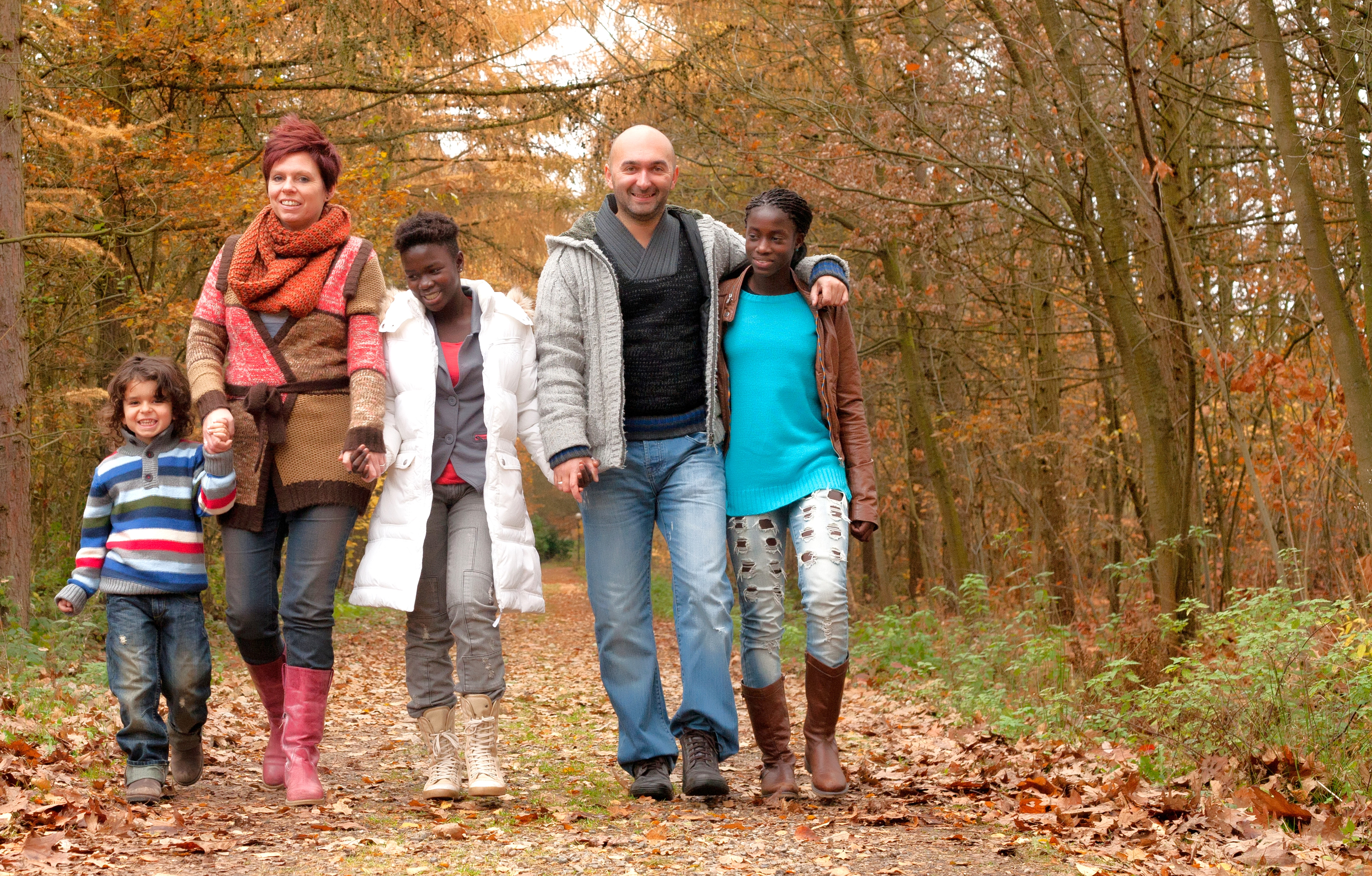 A resource family of 2 adults and three children walk through a forest.