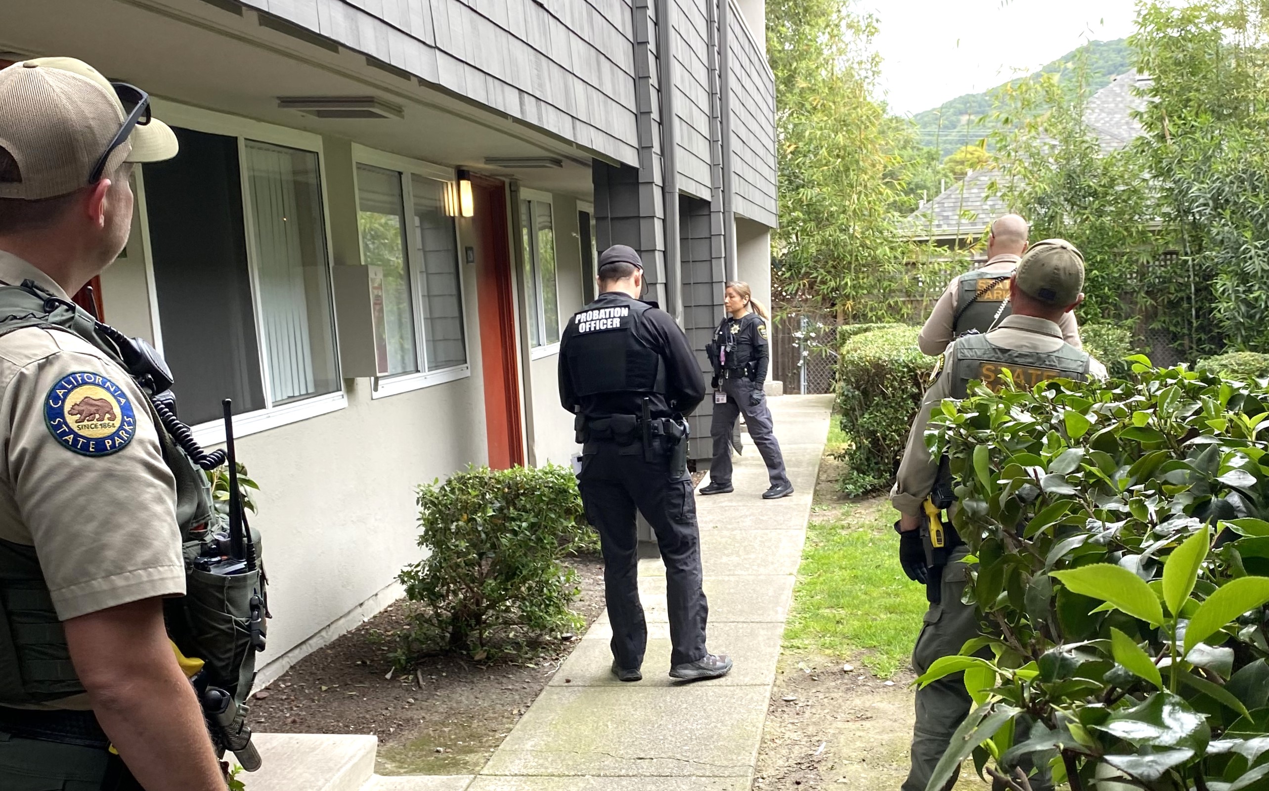 Several law enforcement officers wait outside the apartment door of a person on probation.